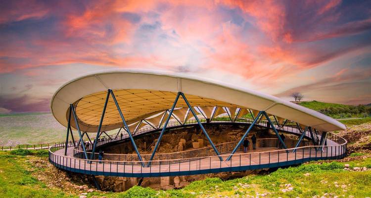 Modern protective canopy over the prehistoric ruins of Göbekli Tepe under a dramatic sunset sky.