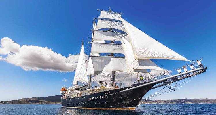 Le navire élancé aux voiles majestueuses se dirige vers l'horizon avec des passagers enthousiastes posant sur le beaupré sous un ciel radieux.