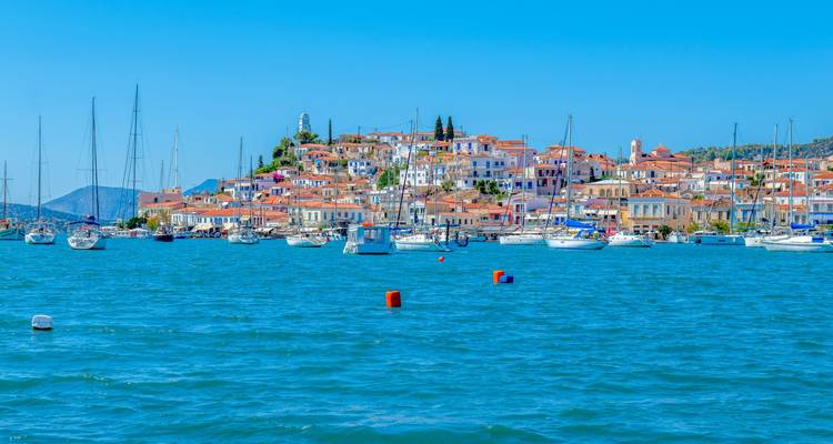 Island town of Poros with orange rooftops viewed across bright blue water filled with sailboats