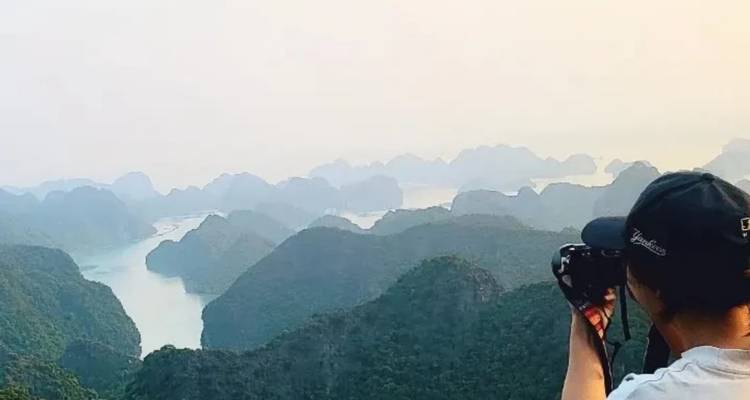 Una joven fotógrafa apunta con su cámara hacia los picos de piedra caliza envueltos en niebla y la bahía sinuosa que se extiende abajo.
