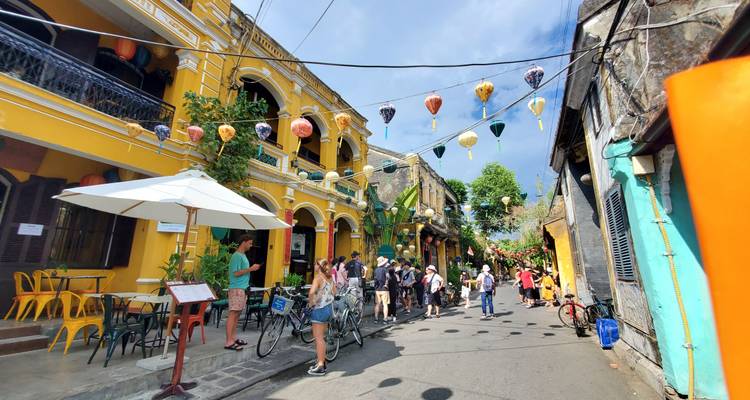 Calle soleada en la Ciudad Antigua de Hoi An, llena de casas amarillas de comerciantes, faroles y ciclistas.