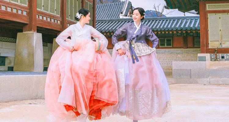 Deux femmes vêtues de hanbok aux couleurs éclatantes posant de manière ludique dans une cour de palais.