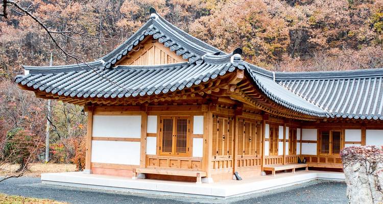 Bâtiment hanok traditionnel avec treillis en bois complexe et toit en tuiles grises entouré d'arbres d'automne.
