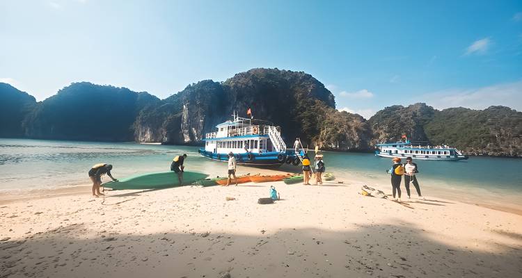 Viajeros descargando kayaks en una playa soleada con barcos de crucero anclados en la bahía