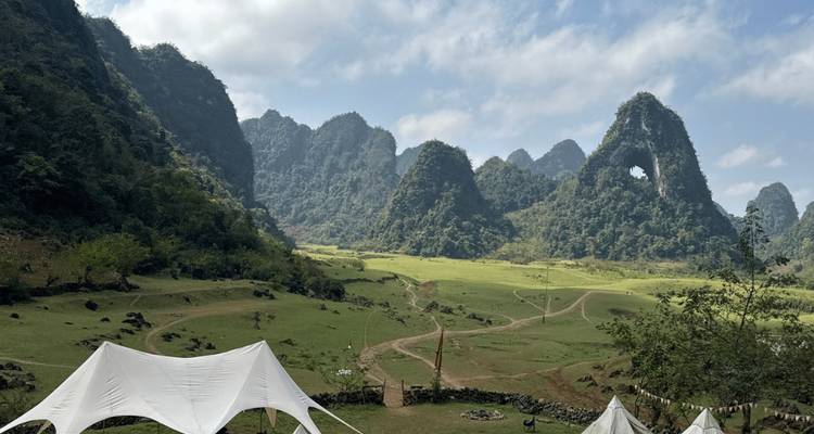 Valle abierto y herboso con picos de karst dramáticos y tiendas de campaña de lona montadas para acampar.
