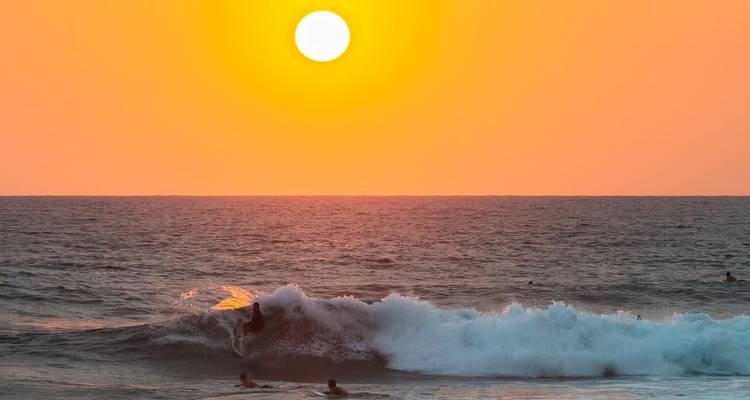 Surfer catches a wave at sunset with a glowing orange sun over the Indian Ocean.