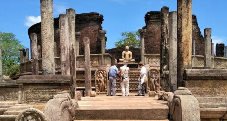 Travelers explore the ancient circular Vatadage ruins in Polonnaruwa under blue skies.