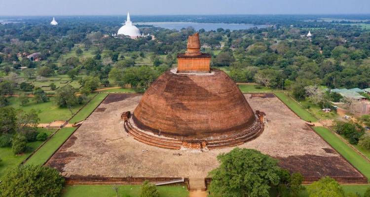 Massive brick stupa rising above green plains in Anuradhapura with distant lakes.