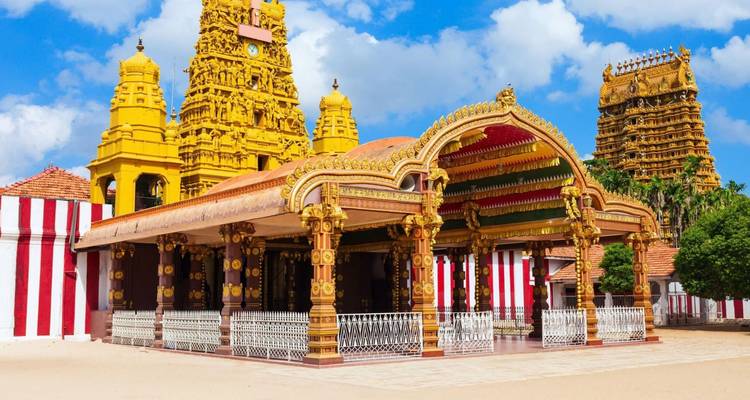 Bright yellow Dravidian-style Hindu temple with striped walls and ornate towers under a blue sky.
