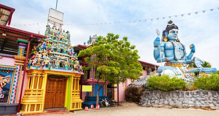 Large blue Shiva statue seated beside a vibrantly painted temple building.