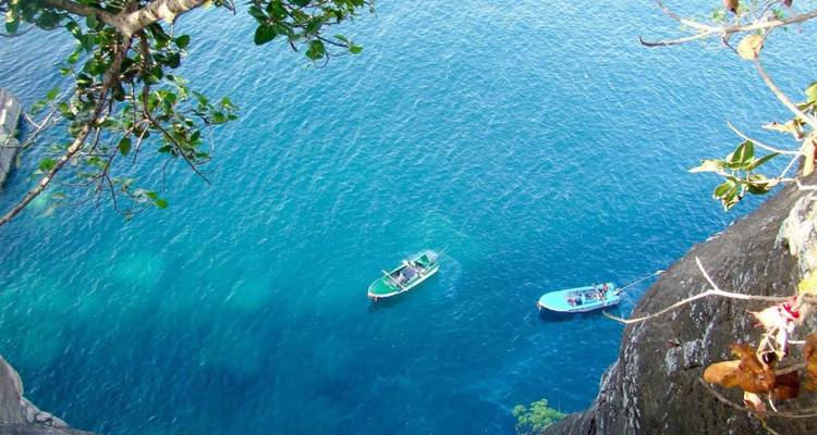 Two small boats float on dazzling turquoise water viewed from a cliff top.