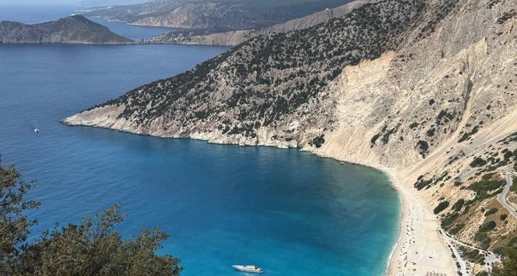 High viewpoint over Myrtos Beach with vivid blue water hugging steep limestone cliffs in Cephalonia.