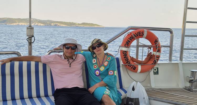 Relaxed couple lounging on a striped bench aboard a yacht with open sea backdrop.