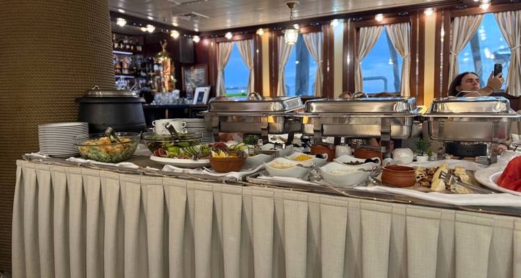Indoor buffet line on a ship with assorted salads, chafing dishes and a passenger taking photos.