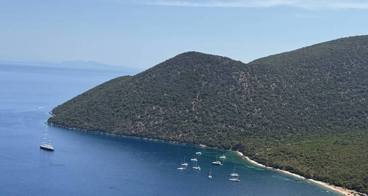 Quiet bay surrounded by forested hills with yachts anchored in deep blue water.