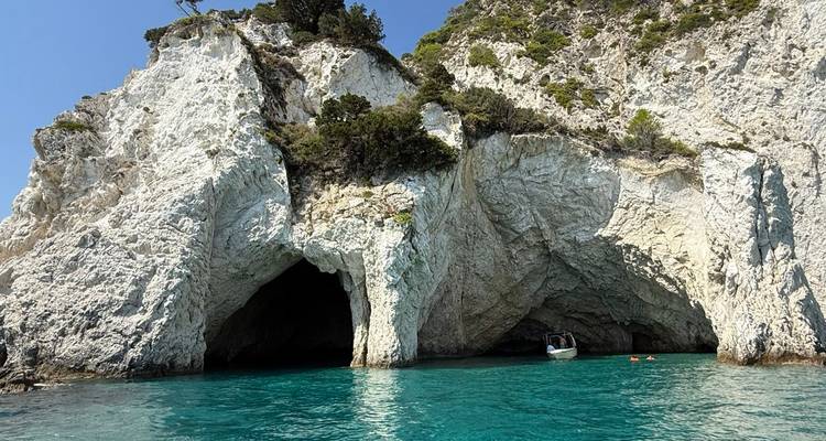 Sea caves with white limestone arches opening onto brilliant turquoise water and a small boat.