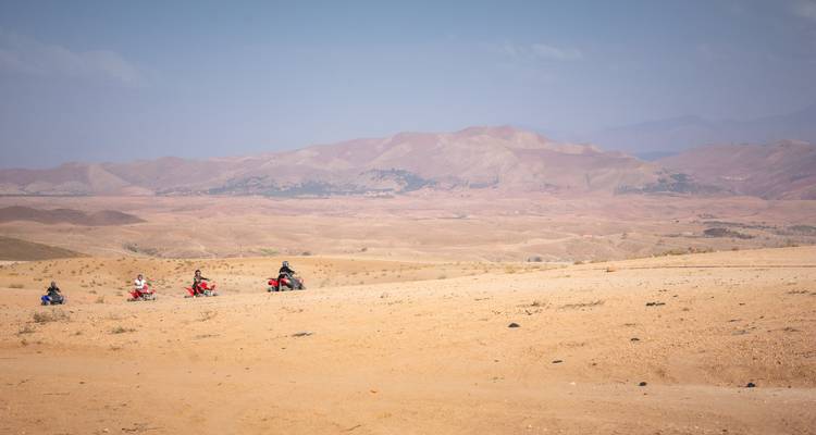 Un petit convoi de quads traversant un vaste plateau aride avec les contreforts de l'Atlas brumeux au-delà.
