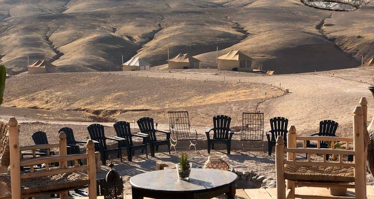 Terrasse du campement du désert avec des rangées de chaises face aux collines dorées ondulantes et aux tentes dispersées.