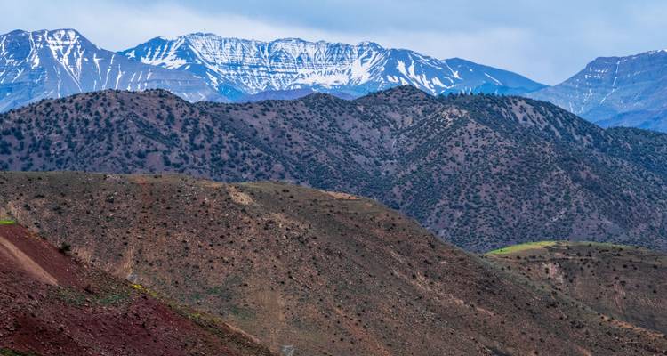 Chaîne de montagnes du Haut Atlas enneigée s'élevant au-dessus de contreforts accidentés aux teintes multiples.