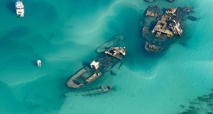 Aerial view of rusting shipwrecks submerged in turquoise waters off the Queensland coast.