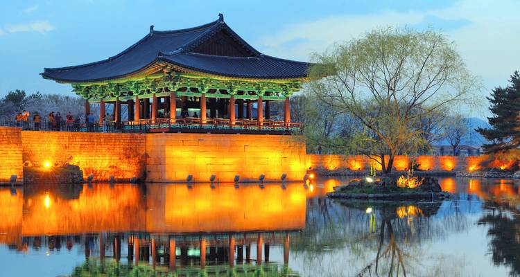 Pavillon illuminé se reflétant dans un étang serein au crépuscule.