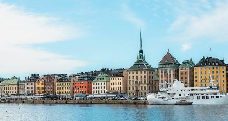 Les façades historiques colorées de la Vieille Ville de Stockholm vues depuis l'autre côté du port avec un bateau de croisière blanc.