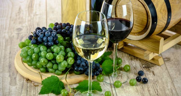 Close-up of white and red wine glasses beside bunches of green and black grapes and a small barrel.