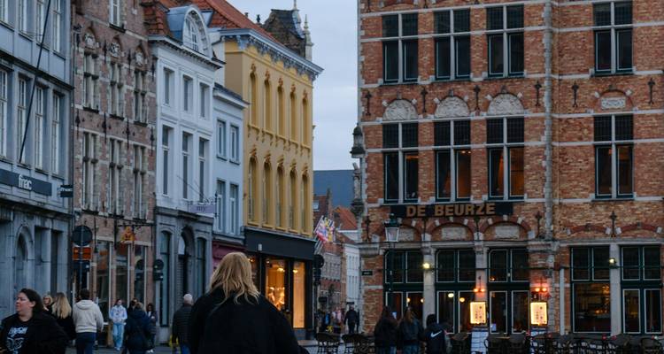 Des bâtiments en brique et en pierre bordent une rue animée à Bruges, avec des piétons et des commerces.