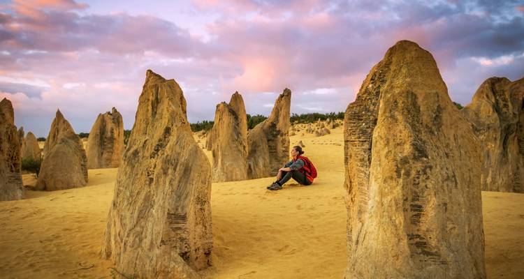 Traveler sits among towering limestone pinnacles in a golden desert at colorful sunset