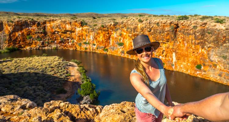 Smiling traveler reaches back for a hand atop a vivid red-rock gorge overlooking a river