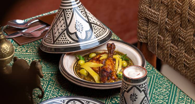 Traditional Moroccan tagine dish served on patterned tablecloth with candle and decor