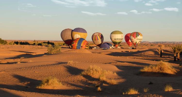Several colourful hot-air balloons inflated over rolling desert dunes at dawn
