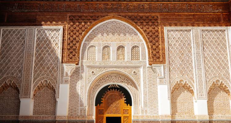 Sun-lit facade of richly decorated Moroccan madrasa with carved wooden arch