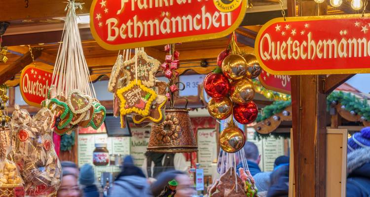 Close-up of gingerbread, bells and ornaments hanging at a German Christmas market stall with blurred shoppers behind