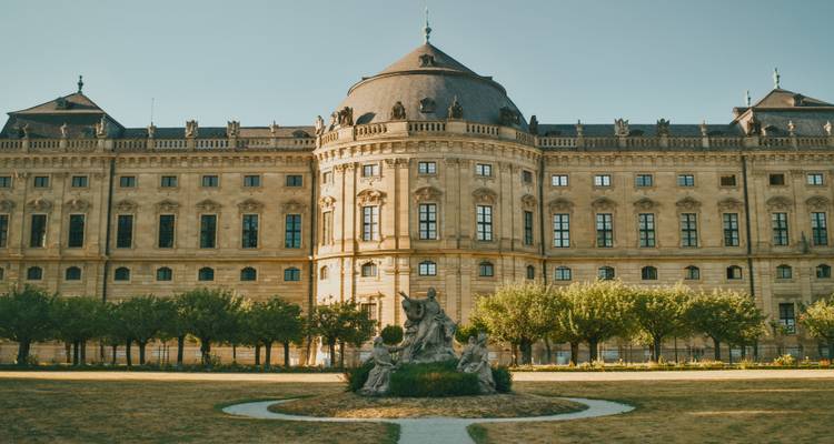 Front facade of the Baroque Würzburg Residence palace with central fountain and trimmed garden under clear sky