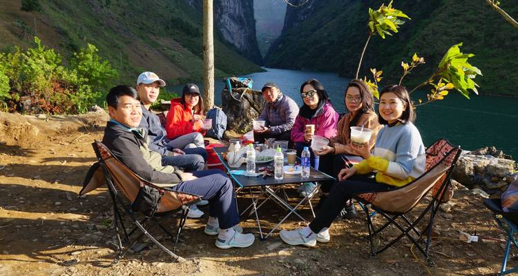 Grupo de amigos disfrutando de un picnic al aire libre alrededor de una mesa baja junto a un cañón de río pintoresco.