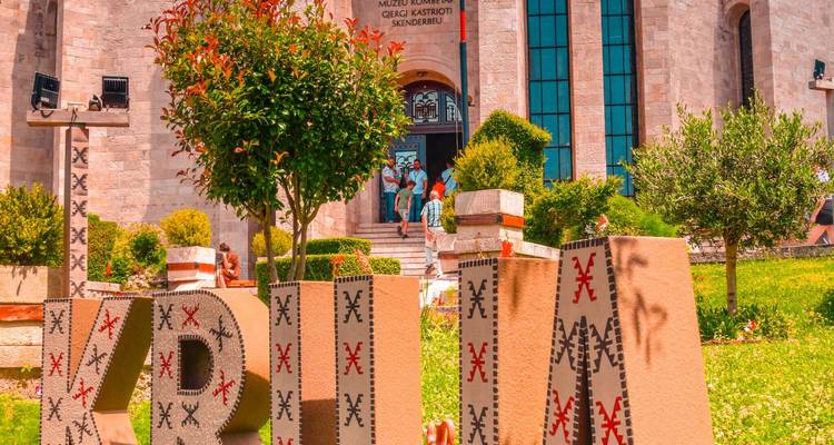 Entrance to Skanderbeg Museum in Krujë with large decorative KRUJA letters and visitors on the steps.