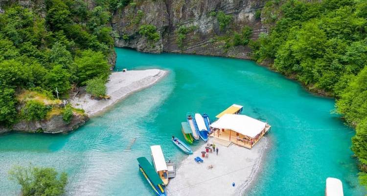 Aerial panorama of vivid turquoise river gorge with boats docked at a sandy islet and steep green cliffs.