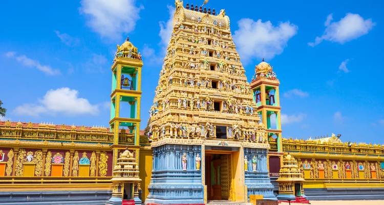 Vibrant golden-yellow gopuram of a Hindu temple rises against a bright blue sky, richly adorned with statues.