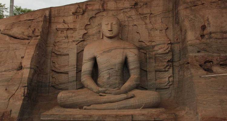 Carved rock Buddha statue sits serenely in meditation posture on a sandstone cliff.