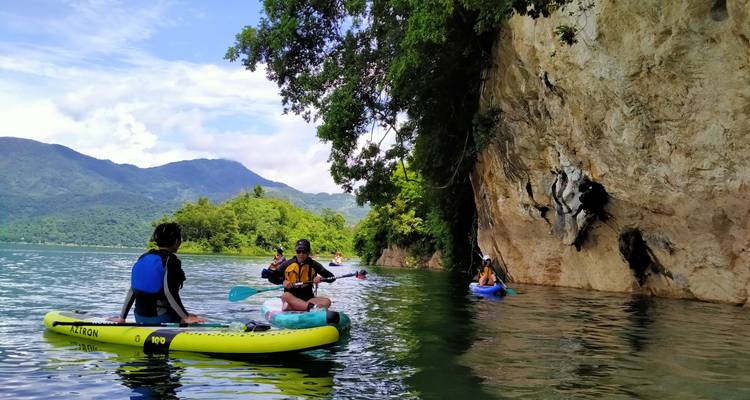 Los remeros en kayaks inflables se deslizan junto a un acantilado rocoso cubierto de vegetación selvática.