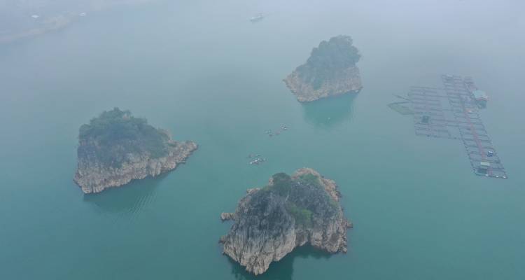 Vista aérea de islotes de piedra caliza envueltos en niebla y kayaks diminutos en un lago turqueso tranquilo.