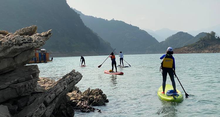 Los practicantes de paddle boarding se lanzan desde una costa rocosa hacia aguas verdes y tranquilas enmarcadas por montañas.
