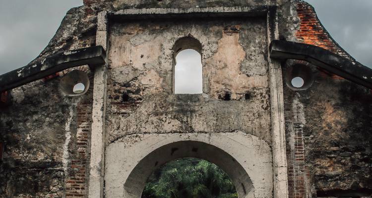 Weathered stone and brick ruins of an old church facade framed by a cloudy sky.