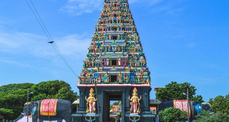 Lebhaft bemalter Eingang eines Hindu-Tempels mit Elefantenstatuen vor klarem blauen Himmel.