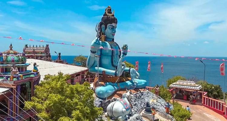 Riesige türkisfarbene Shiva-Statue mit Blick auf den Indischen Ozean mit Tempelanlage darunter.