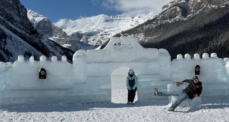 Travellers pose and play around an ice castle on a frozen mountain lake.