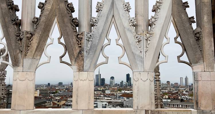 Les flèches en marbre ouvragé de la terrasse du Duomo encadrant l'horizon urbain moderne de Milan en dessous.