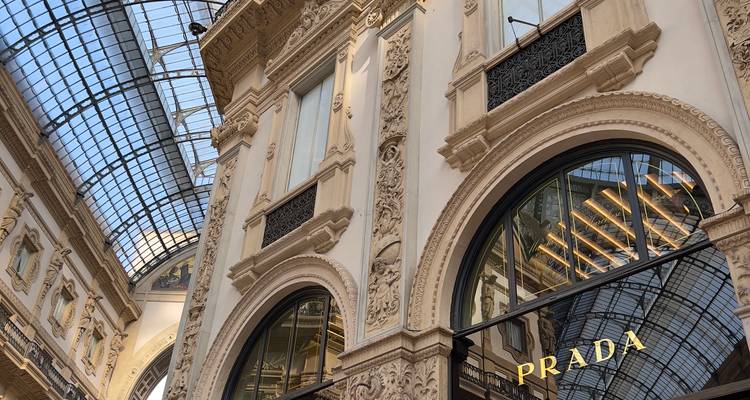 Intérieur de la Galerie Vittorio Emanuele II avec des stuccos ornés et une devanture Prada sous un toit en verre.