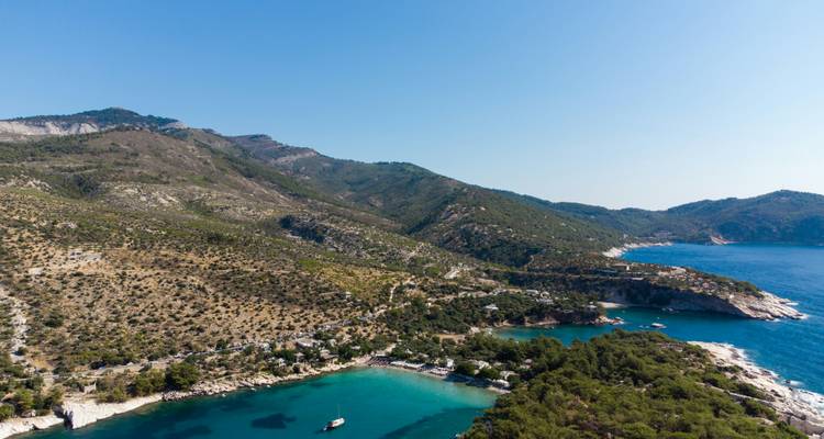 Vue aérienne d'une baie turquoise abritée bordée de forêts de pins et de montagnes escarpées sur l'île de Thassos.